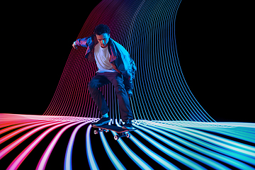 Image showing Caucasian young skateboarder riding on dark neon lighted line background