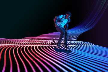 Image showing Caucasian young skateboarder riding on dark neon lighted line background