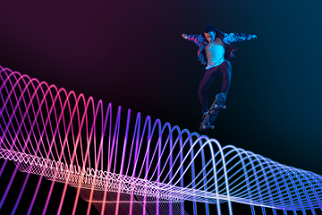 Image showing Caucasian young skateboarder riding on dark neon lighted line background