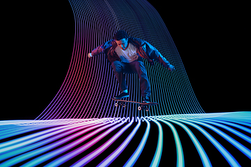 Image showing Caucasian young skateboarder riding on dark neon lighted line background