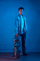 Image showing Caucasian young skateboarder posing on dark neon lighted background