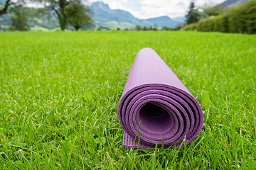 Image showing Rolled up fitness mat on the green grass background