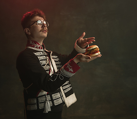 Image showing Young man in suit as royal person isolated on dark green background. Retro style, comparison of eras concept. Beautiful male model like historical character, monarch, old-fashioned.