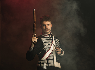 Image showing Young man in suit as royal person isolated on dark green background. Retro style, comparison of eras concept. Beautiful male model like historical character, monarch, old-fashioned.