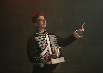 Image showing Young man in suit as royal person isolated on dark green background. Retro style, comparison of eras concept. Beautiful male model like historical character, monarch, old-fashioned.