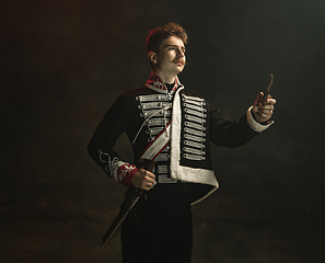 Image showing Young man in suit as royal person isolated on dark green background. Retro style, comparison of eras concept. Beautiful male model like historical character, monarch, old-fashioned.