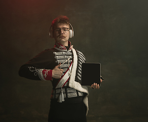 Image showing Young man in suit as royal person isolated on dark green background. Retro style, comparison of eras concept. Beautiful male model like historical character, monarch, old-fashioned.