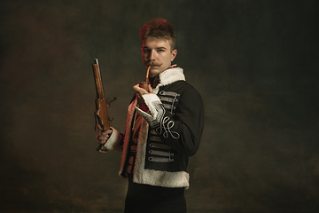 Image showing Young man in suit as royal person isolated on dark green background. Retro style, comparison of eras concept. Beautiful male model like historical character, monarch, old-fashioned.