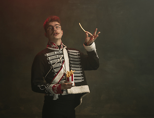 Image showing Young man in suit as royal person isolated on dark green background. Retro style, comparison of eras concept. Beautiful male model like historical character, monarch, old-fashioned.