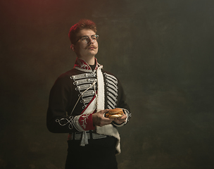 Image showing Young man in suit as royal person isolated on dark green background. Retro style, comparison of eras concept. Beautiful male model like historical character, monarch, old-fashioned.