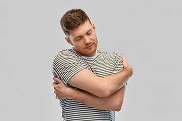 Image showing happy young man in striped t-shirt hugging himself