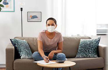 Image showing woman in mask with papers and calculator at home