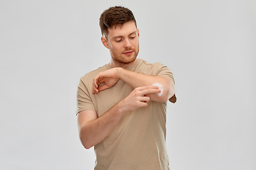 Image showing young man applying pain medication to his elbow