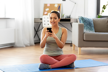 Image showing woman with smartphone sits on exercise mat at home