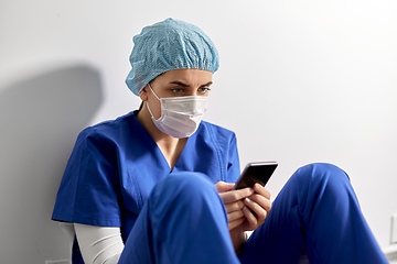 Image showing sad doctor or nurse in face mask with smartphone
