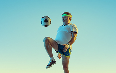 Image showing Senior man playing football in sportwear on gradient background and neon light