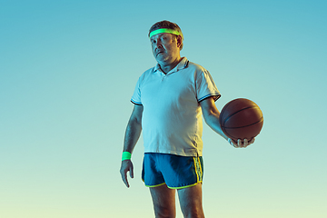 Image showing Senior man playing basketball in sportwear on gradient background and neon light