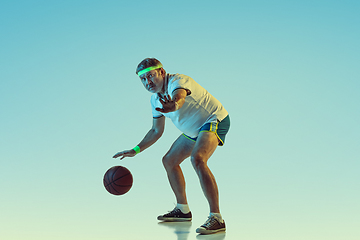 Image showing Senior man playing basketball in sportwear on gradient background and neon light