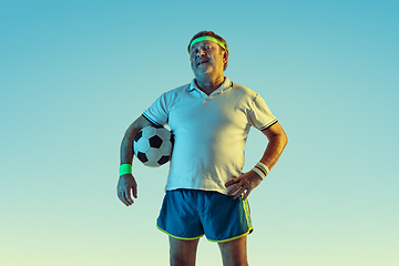 Image showing Senior man playing football in sportwear on gradient background and neon light
