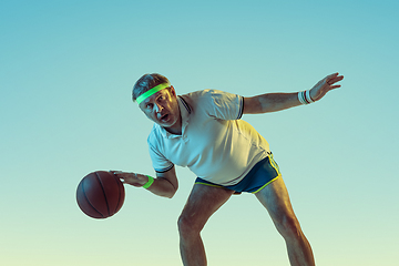 Image showing Senior man playing basketball in sportwear on gradient background and neon light