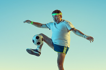 Image showing Senior man playing football in sportwear on gradient background and neon light