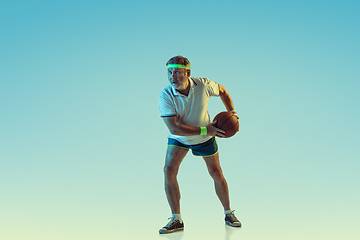 Image showing Senior man playing basketball in sportwear on gradient background and neon light