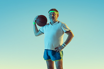 Image showing Senior man playing basketball in sportwear on gradient background and neon light