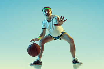 Image showing Senior man playing basketball in sportwear on gradient background and neon light