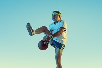 Image showing Senior man playing basketball in sportwear on gradient background and neon light