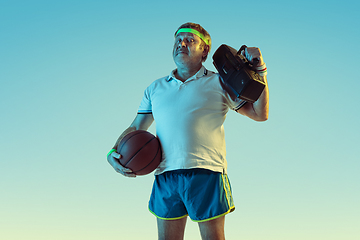 Image showing Senior man posing stunning in sportwear with retro tape recorder on gradient background and neon light