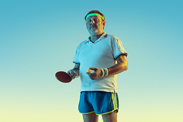 Image showing Senior man playing table tennis in sportwear on gradient background and neon light