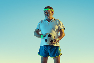 Image showing Senior man playing football in sportwear on gradient background and neon light