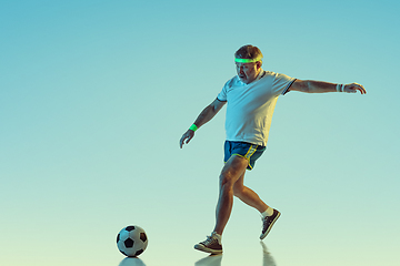 Image showing Senior man playing football in sportwear on gradient background and neon light