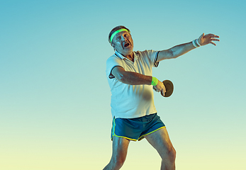 Image showing Senior man playing table tennis in sportwear on gradient background and neon light