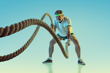 Image showing Senior man training with ropes in sportwear on gradient background and neon light