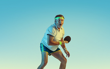 Image showing Senior man playing table tennis in sportwear on gradient background and neon light