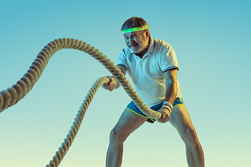 Image showing Senior man training with ropes in sportwear on gradient background and neon light