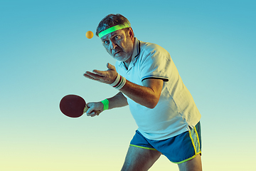 Image showing Senior man playing table tennis in sportwear on gradient background and neon light