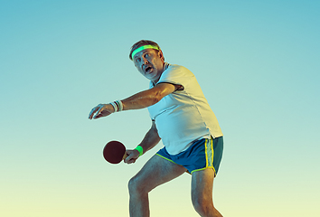 Image showing Senior man playing table tennis in sportwear on gradient background and neon light