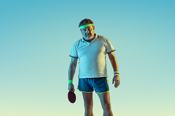 Image showing Senior man playing table tennis in sportwear on gradient background and neon light