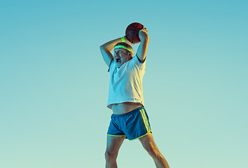 Image showing Senior man playing basketball in sportwear on gradient background and neon light