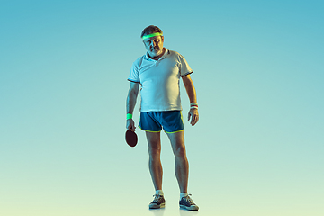 Image showing Senior man playing table tennis in sportwear on gradient background and neon light