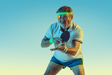 Image showing Senior man playing table tennis in sportwear on gradient background and neon light