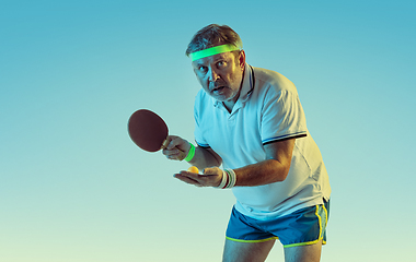 Image showing Senior man playing table tennis in sportwear on gradient background and neon light