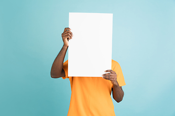 Image showing Young African man with blank sheet of paper isolated over blue studio background.