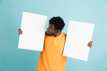 Image showing Young African man with blank sheets of paper isolated over blue studio background.