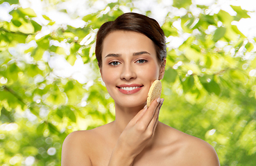 Image showing young woman cleaning face with exfoliating sponge