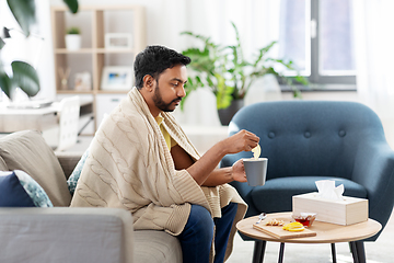 Image showing sick young man in blanket drinking hot tea at home