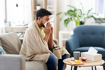 Image showing sick man blowing nose in paper tissue at home