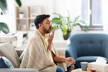 Image showing sick young man in blanket coughing at home